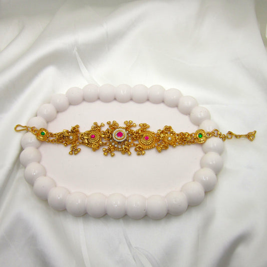 Alankrita Luxe Heritage Bracelet by Enava featuring antique gold finish, ruby pink and emerald green stones, pearl accents, intricate traditional floral motifs, adjustable chain closure, and a premium heritage bracelet for weddings, festive occasions, and bridal wear.