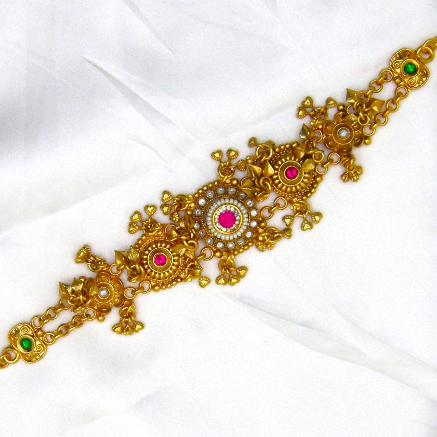 Alankrita Luxe Heritage Bracelet by Enava featuring antique gold finish, ruby pink and emerald green stones, pearl accents, intricate traditional floral motifs, adjustable chain closure, and a premium heritage bracelet for weddings, festive occasions, and bridal wear.