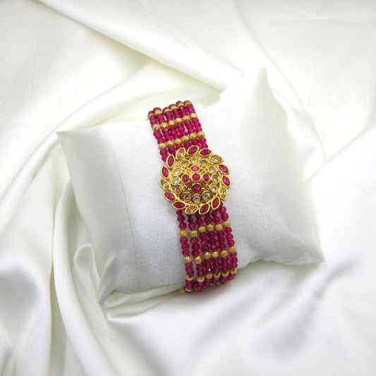 Ruhanika Ruby Pink Ethnic Bracelet by Enava featuring multi-strand ruby pink crystal beads, antique gold floral centerpiece, American Diamond detailing, adjustable chain closure, handcrafted ethnic design, and a premium statement bracelet for weddings, festive occasions, traditional wear, and party styling.