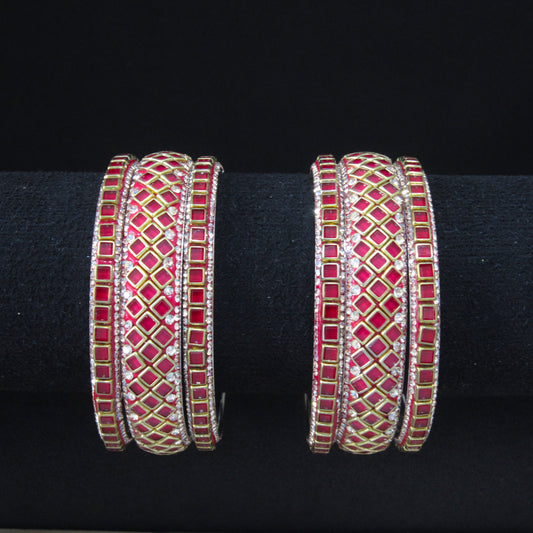 A pair of gold-plated bangles decorated with red and white enamel geometric patterns and set with small clear stones, displayed on a black velvet ring stand.