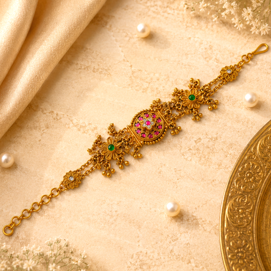 Alankrita Royal Ruby Pink Bracelet by Enava featuring antique gold finish, ruby pink stones, emerald green floral accents, American Diamond detailing, intricate heritage craftsmanship, hanging traditional charms, adjustable chain closure, and a premium ethnic statement bracelet for weddings, festive occasions, and bridal wear.