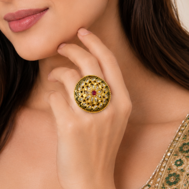 A close-up lifestyle shot of a woman wearing a large, ornate gold ring with intricate green and white stone detailing and a central red gemstone.