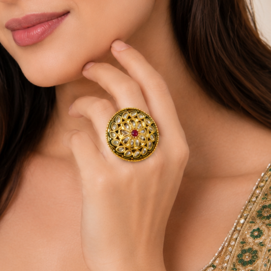 A close-up lifestyle shot of a woman wearing a large, ornate gold ring with intricate green and white stone detailing and a central red gemstone.