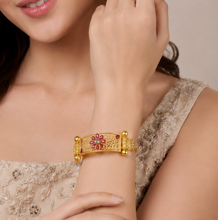 A close-up of a woman wearing a gold-plated traditional Indian-style bracelet with red and green floral engravings on her wrist.