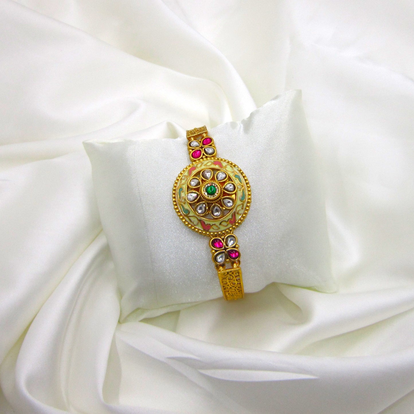 Kalashini Enamel Ethnic Bracelet by Enava featuring a circular Kundan centerpiece with hand-painted ivory Meenakari enamel, emerald green center stone, ruby pink floral accents, antique gold finish, adjustable closure, and a premium ethnic statement bracelet for weddings and festive occasions.