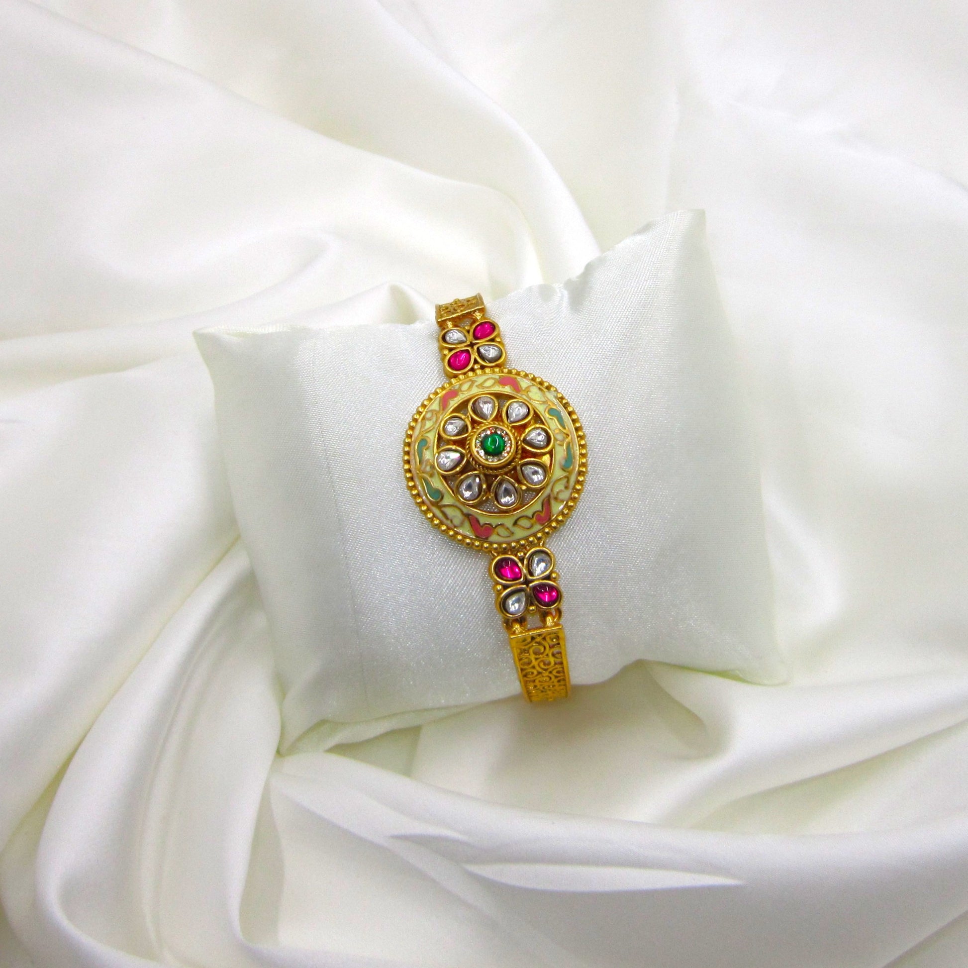 Kalashini Enamel Ethnic Bracelet by Enava featuring a circular Kundan centerpiece with hand-painted ivory Meenakari enamel, emerald green center stone, ruby pink floral accents, antique gold finish, adjustable closure, and a premium ethnic statement bracelet for weddings and festive occasions.