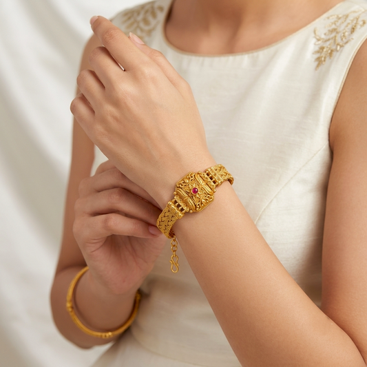 Kusum Heritage Rajwadi Bracelet by ENAVA featuring antique gold finish, floral centerpiece, ruby red stone accent, and intricate braided Rajwadi craftsmanship for weddings and festive wear.