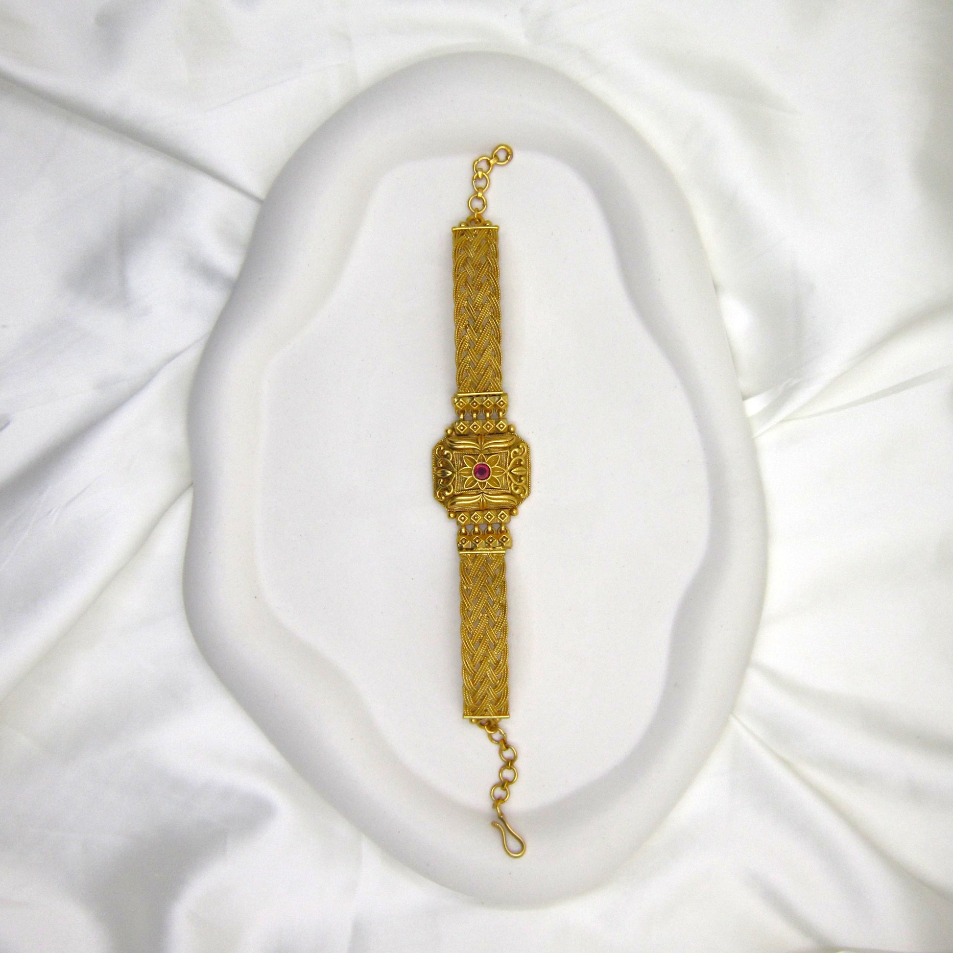 Kusum Heritage Rajwadi Bracelet by ENAVA featuring antique gold finish, floral centerpiece, ruby red stone accent, and intricate braided Rajwadi craftsmanship for weddings and festive wear.