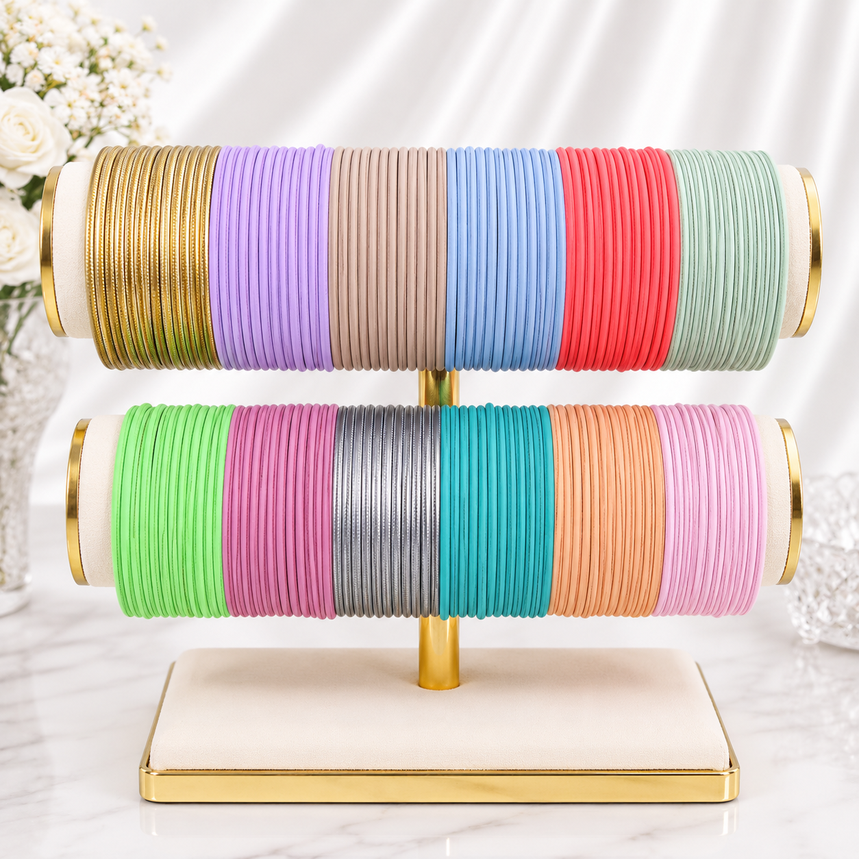 A jewelry display stand holding two horizontal rows of colorful elastic bangles. The stand has a cream-colored base with gold trim and a gold central post.