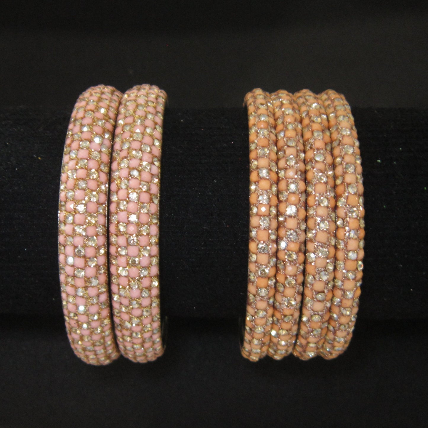 Two sets of beaded bangles displayed on a black velvet jewelry stand. The left set consists of two wide bands covered in light pink square beads with small clear rhinestones.