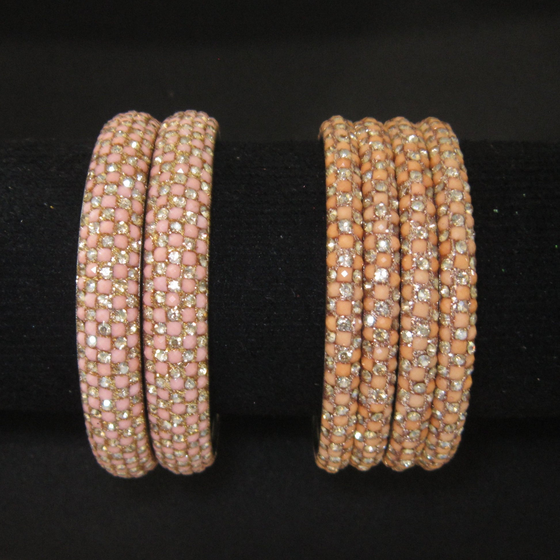 Two sets of beaded bangles displayed on a black velvet jewelry stand. The left set consists of two wide bands covered in light pink square beads with small clear rhinestones.