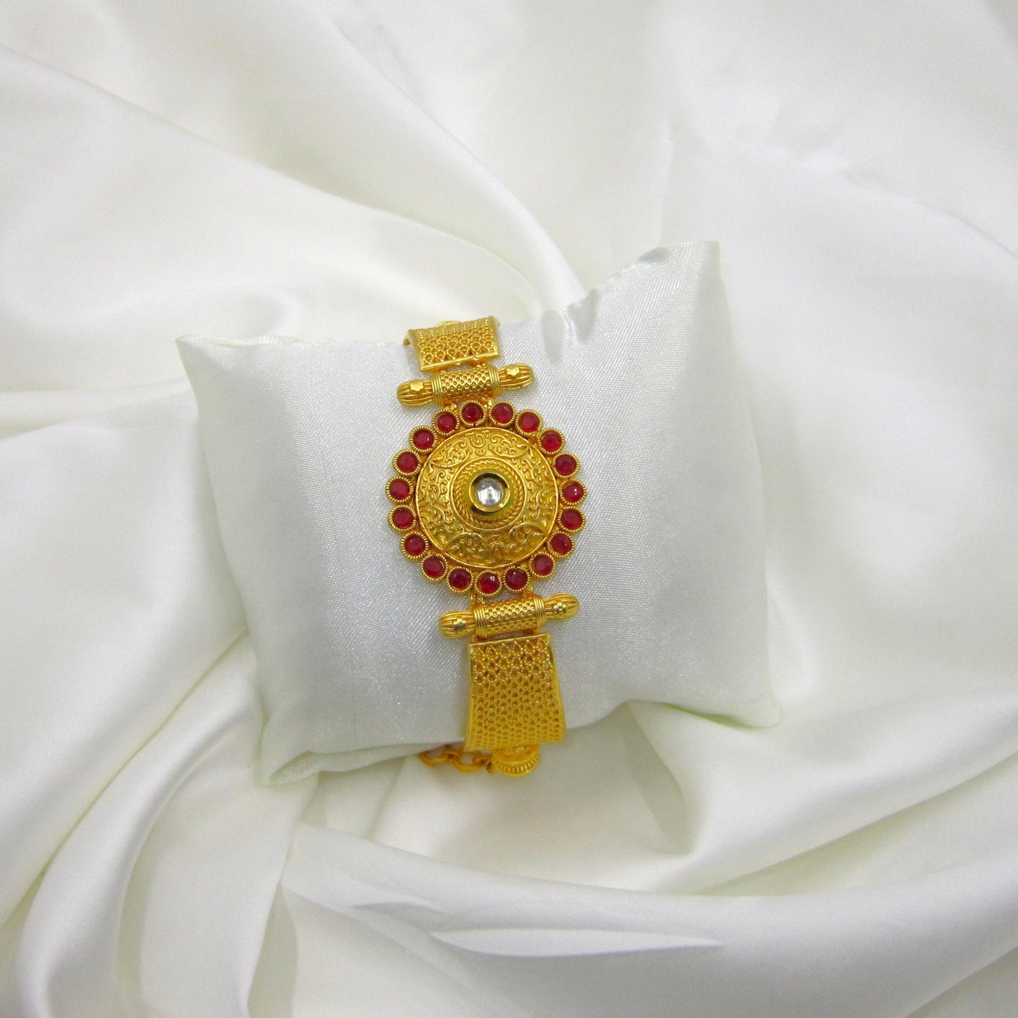 Mrinalini Ruby Golden Bracelet by Enava featuring an engraved antique gold circular centerpiece with a mirror stone, ruby red crystal border, textured mesh band, adjustable chain closure, premium ethnic statement bracelet for weddings and festive wear.
