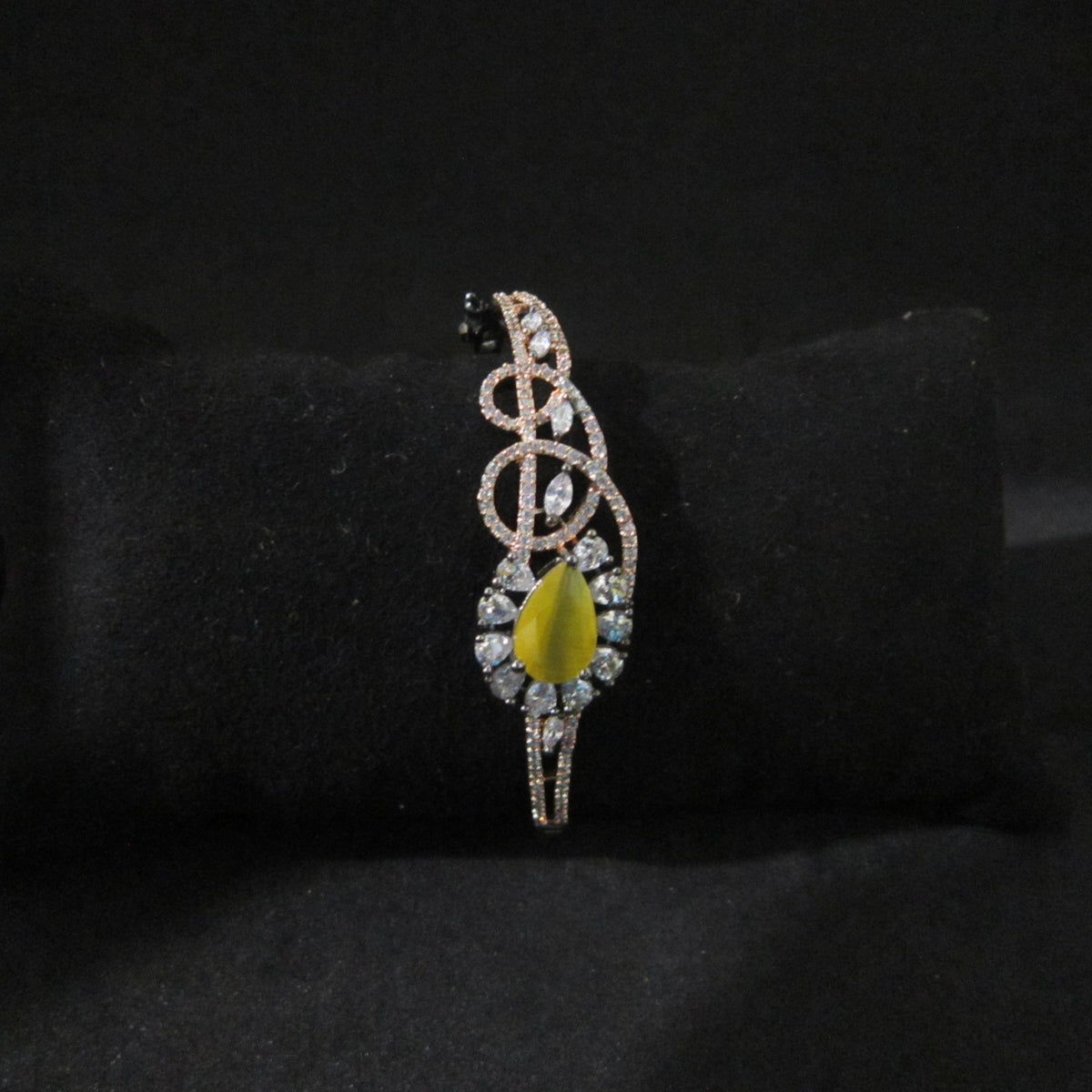 A decorative brooch with a yellow-green teardrop center stone, surrounded by clear rhinestones in a silver-toned setting, displayed on a black velvet ring stand.