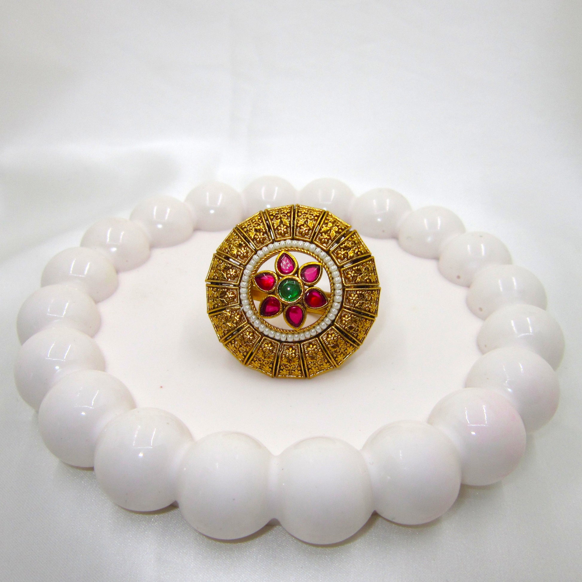 Pushpika Heritage Floral Antique Golden Finish Ethnic Ring by Enava featuring ruby pink teardrop glass stones, emerald green centre stone, pearl bead detailing, intricate floral motif, adjustable statement ring for weddings, festive wear, and traditional ethnic jewellery.