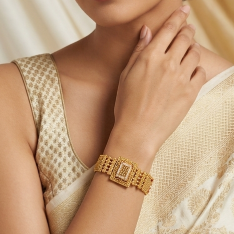 A close-up of a woman wearing a gold-toned rectangular link bracelet with a central stone, paired with a cream-colored patterned blouse.