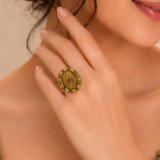 A close-up lifestyle shot of a woman's hand wearing an ornate vintage-style gold ring with a central red gemstone.
