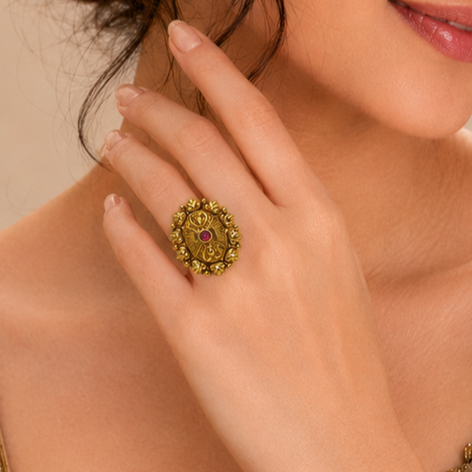 A close-up lifestyle shot of a woman's hand wearing an ornate vintage-style gold ring with a central red gemstone.