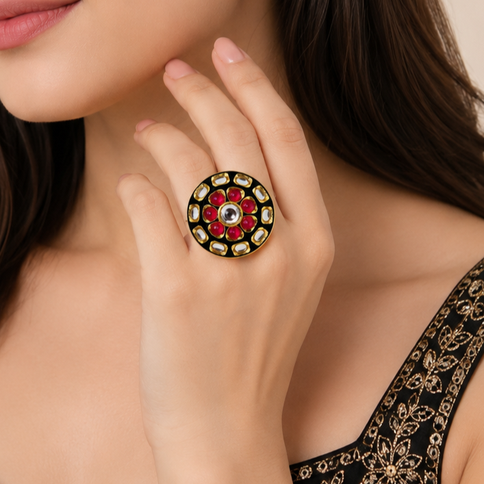 A close-up lifestyle shot of a woman wearing a large, round gold ring decorated with a red and white floral pattern and clear stones.