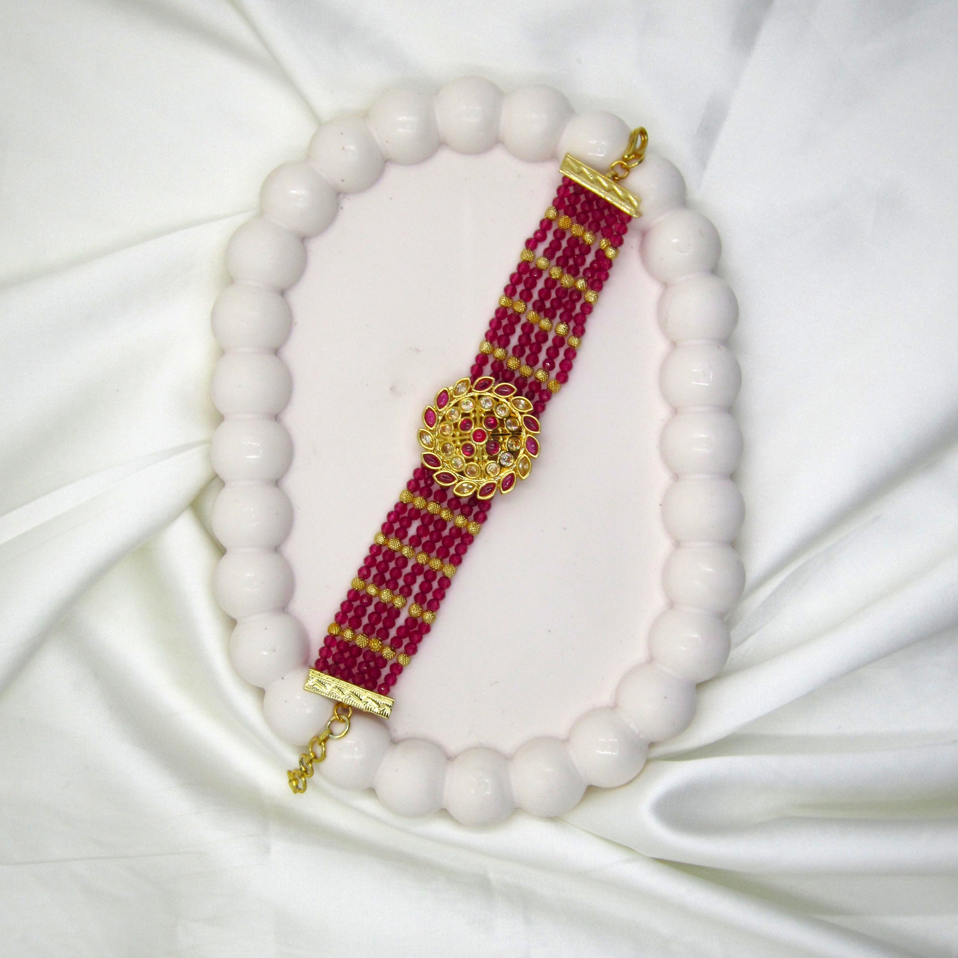 Ruhanika Ruby Pink Ethnic Bracelet by Enava featuring multi-strand ruby pink crystal beads, antique gold floral centerpiece, American Diamond detailing, adjustable chain closure, handcrafted ethnic design, and a premium statement bracelet for weddings, festive occasions, traditional wear, and party styling.