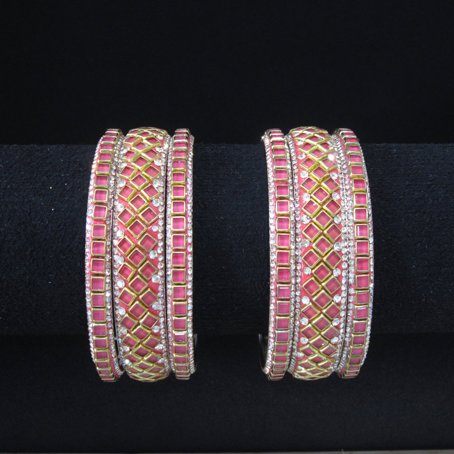 Four wide silver-toned bangles decorated with pink rectangular stones and gold diamond-pattern inlays, displayed on a black background.