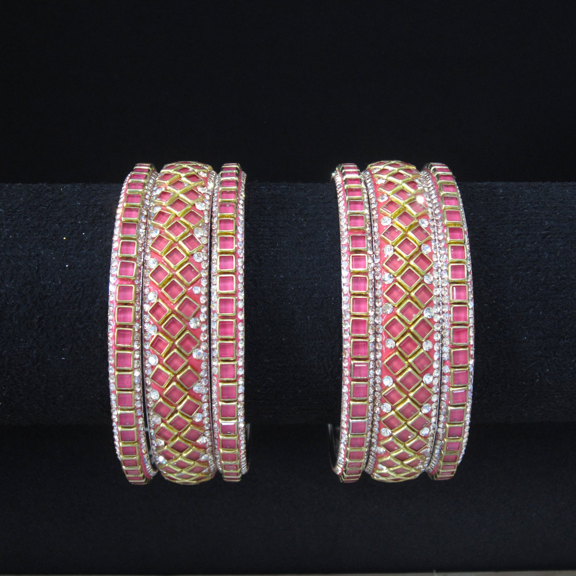 Four wide silver-toned bangles decorated with pink rectangular stones and gold diamond-pattern inlays, displayed on a black background.