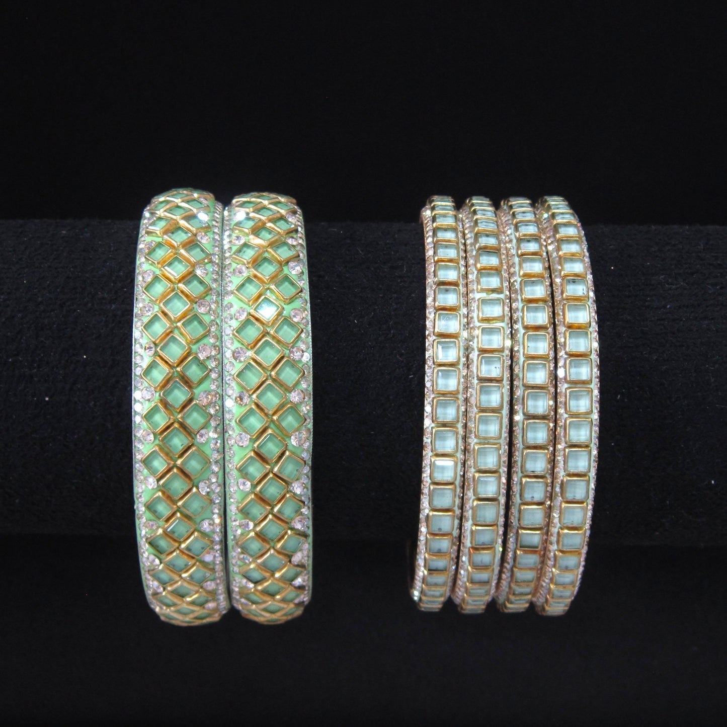 Two sets of gold bangles with light green and white stones, displayed on a black background.