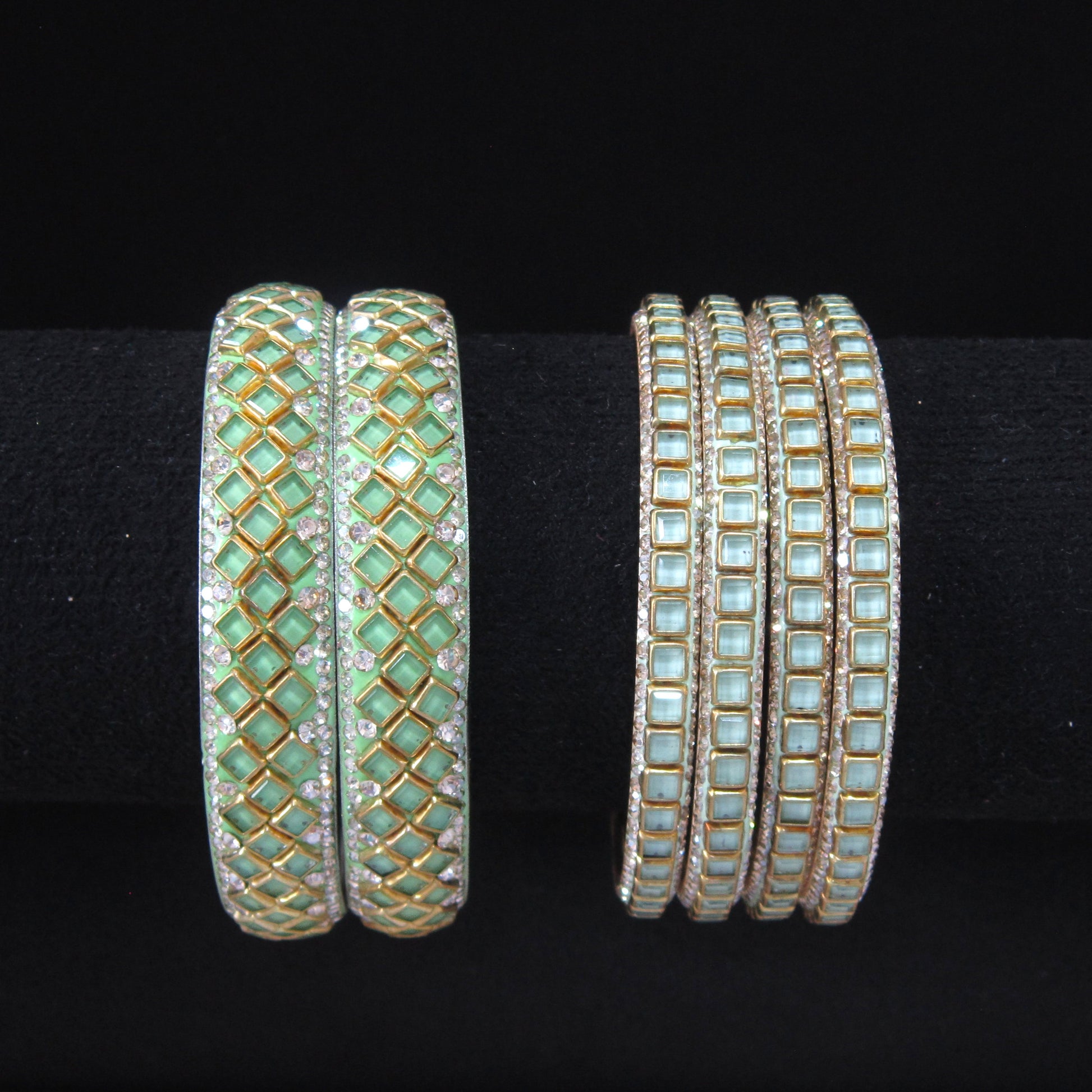 Two sets of gold bangles with light green and white stones, displayed on a black background.