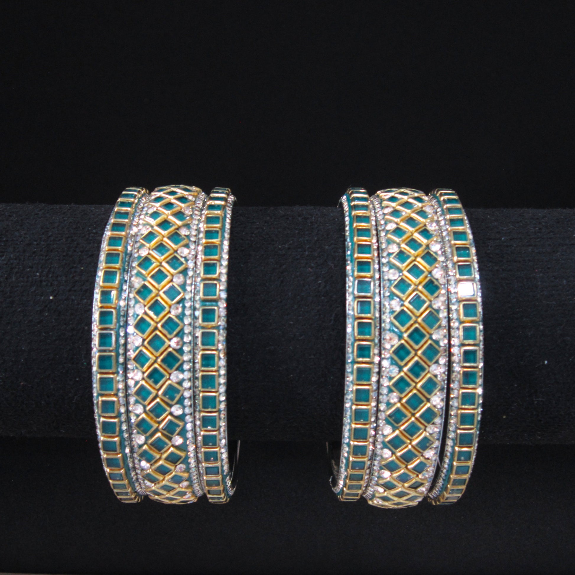 A pair of gold-plated multi-band bangles decorated with turquoise blue stones and clear rhinestones, displayed on a black velvet jewelry stand.