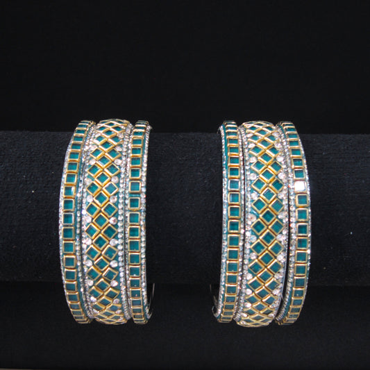 A pair of gold-plated multi-band bangles decorated with turquoise blue stones and clear rhinestones, displayed on a black velvet jewelry stand.