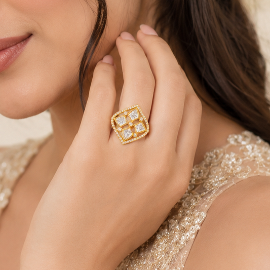 A close-up lifestyle shot of a woman wearing a gold square ring with four clear gemstones, resting her hand near her face.